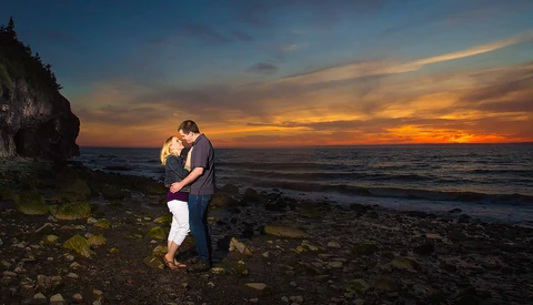 engaged couple embracing on rocky beach at sunset