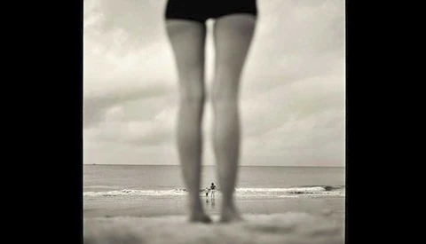 child and adult framed by woman's legs on beach