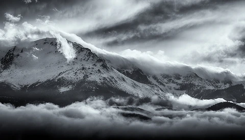 Snow-covered mountain peak shrouded in dramatic storm clouds and mist.
