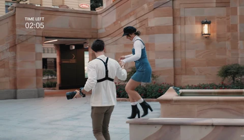 Two people jumping in an urban courtyard with a 2:05 countdown timer overlay.
