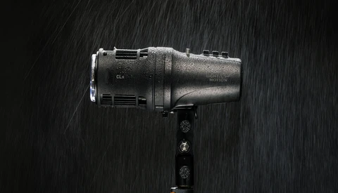 Studio flash unit mounted on a bracket, covered in water droplets against a dark background with rain streaks.