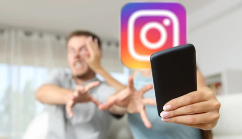 Man giving thumbs-down gesture with smartphone in foreground and Instagram logo in background.