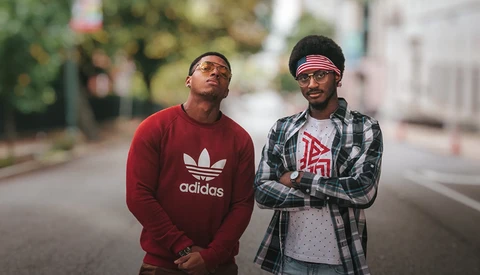 Two men standing on a street wearing casual sportswear and sunglasses.