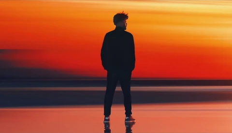 Silhouetted jogger standing on a reflective surface at sunset, facing the horizon.