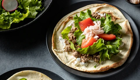 Plated taco with shredded meat, lettuce, tomato, and white crema on a dark round plate.