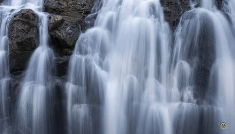 Cascading waterfall flowing over dark rocky terrain with silky water motion blur effect.