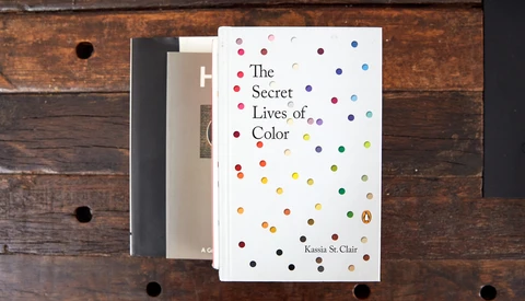 Stack of three books on wooden surface, with 'The Secret Lives of Color' by Kassia St. Clair prominently displayed on top featuring colorful dots.