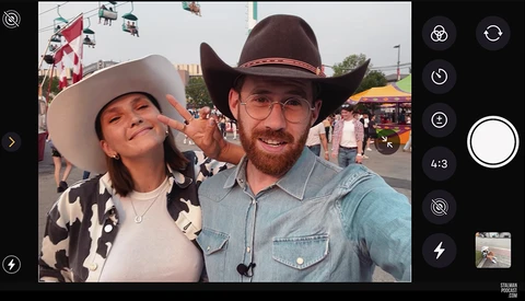 Two people in cowboy hats at a fairground during daytime, smiling at camera.
