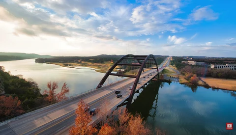 Aerial view of a modern bridge spanning a calm reservoir with forested banks and autumn foliage.
