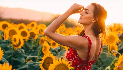 Woman in red dress posing in sunflower field at golden hour.
