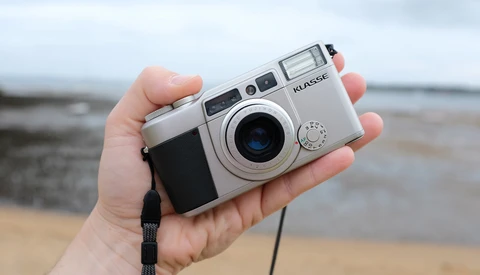 Silver rangefinder camera held in hand against a blurred coastal background.