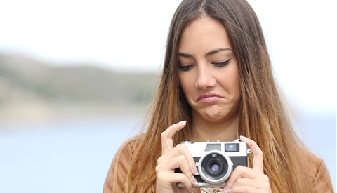Woman holding a rangefinder camera while looking down with a contemplative expression.