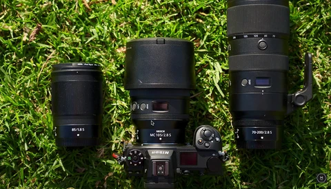 Camera body with three interchangeable lenses arranged on moss-covered ground.