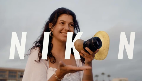 Female photographer holding a camera and gold reflector against sky backdrop.
