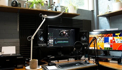 Professional video editing workspace with dual monitors, mixing console, studio speakers, and articulating desk lamp.