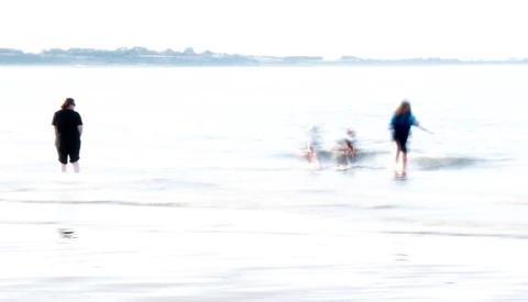 Multiple people wading in shallow ocean water with motion blur effect.