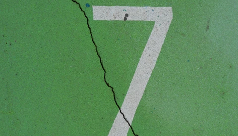 White painted number 7 on green asphalt with a diagonal crack running through it.