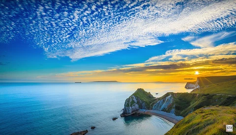 Coastal cliffs with natural stone arch at sunset over calm blue ocean.