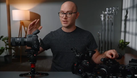 Videographer demonstrating camera equipment and gimbal stabilizer in studio setting.