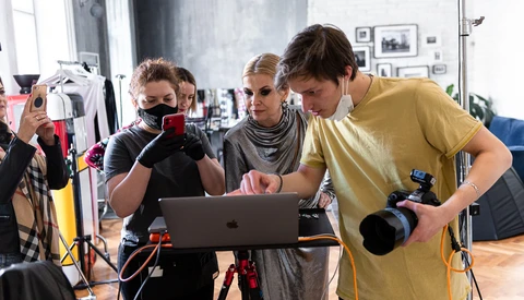 Group of photographers reviewing footage on a laptop during a studio production shoot.