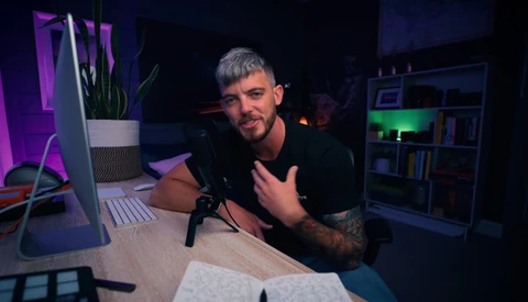 Content creator speaking into microphone at desk with studio lighting setup.