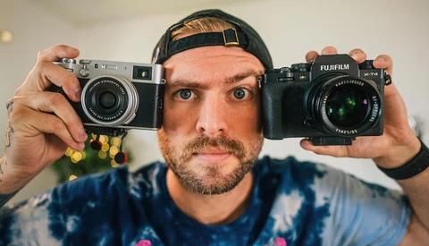 Photographer holding a rangefinder film camera and a Fujifilm mirrorless camera side by side.