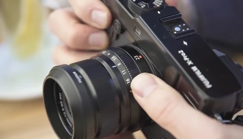 Hands holding a mirrorless camera with a prime lens attached, demonstrating proper grip and handling.