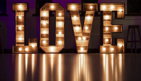 Illuminated marquee-style LOVE sign with warm bulbs against purple backdrop.