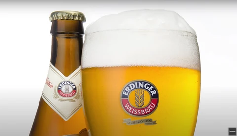 Erdinger Weissbräu beer bottle and glass with thick foam head against white background.