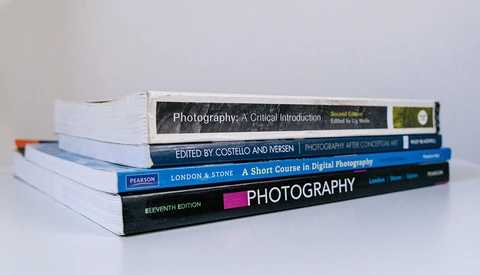 Stack of photography textbooks arranged diagonally on white surface.