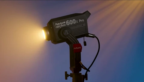 Aputure 600d Pro LED light mounted on stand against gradient blue and orange background.