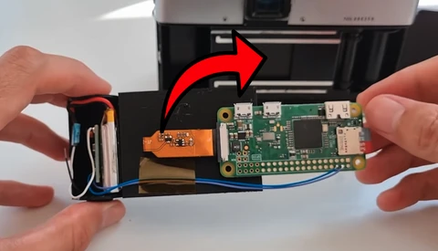 Hands holding open a camera or imaging device to reveal internal circuit boards and battery components.