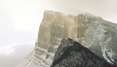 Snow-covered mountain ridge with dramatic layered rock formations and steep cliff faces.