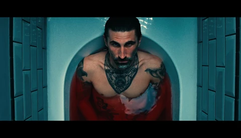 Shirtless man with tattoos and bandana in symmetrical pose under teal circular backdrop.