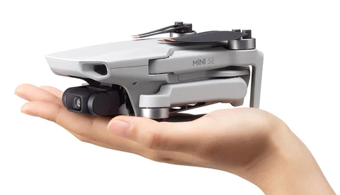 DJI Mini SE drone resting in an open palm, showing compact white and gray body with folded propeller arms.