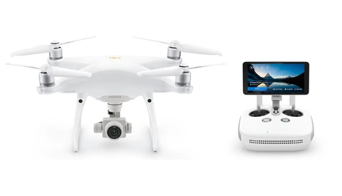 White quadcopter drone with camera gimbal positioned next to its remote controller with integrated smartphone holder.