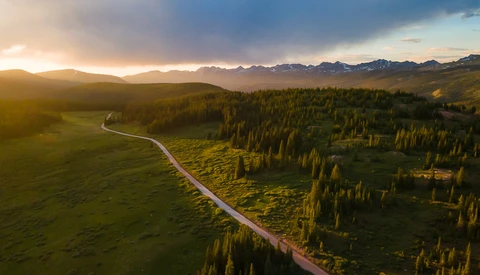 Aerial view of a winding river cutting through forested valley at golden hour with mountains in the distance.