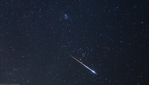 Bright meteor streaking diagonally across a starfield with a blue-white ionized tail.