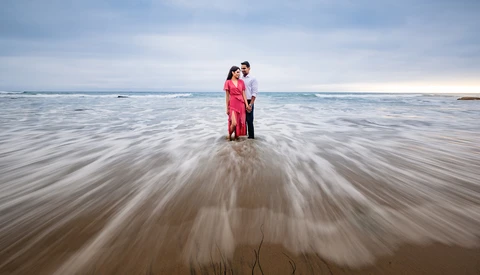 Couple standing in shallow ocean water with long exposure effect showing motion blur of waves.