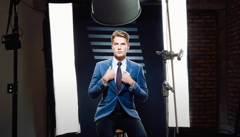 Professional headshot of a man in blue blazer and red tie against striped backdrop with studio lighting.