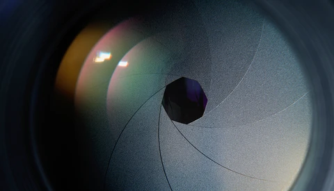 Camera lens aperture opening with bokeh light reflections in the background.