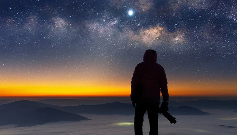 Silhouetted figure standing on a mountain ridge gazing at the Milky Way galaxy at night.