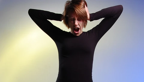 Person in black long-sleeve shirt with hands behind head, mouth open in an excited expression against a gradient blue and yellow background.
