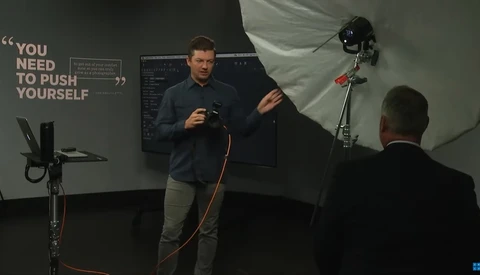 Man speaking during photography workshop with studio lighting setup visible in background.