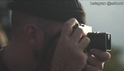 Photographer holding a compact camera up to their face, composing a shot with natural backlighting.