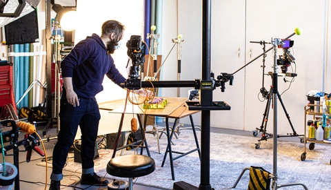 Photographer adjusting a camera on a tripod in a studio with multiple lighting rigs and equipment.