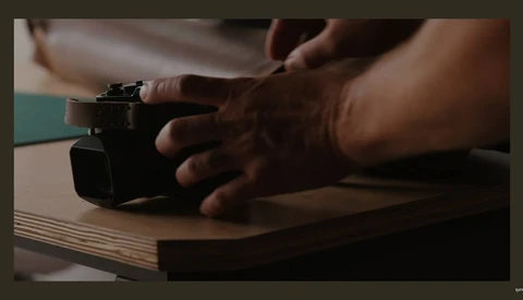 Hands demonstrating operation of a compact camera on a wooden surface.