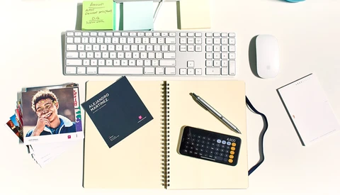 Flat lay of a creative workspace with keyboard, mouse, notebook, calculator, and sticky notes on a neutral background.