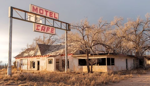 Abandoned motel and cafe with weathered wooden structures and vintage signage in desert landscape.