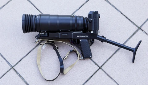 Fotograper film camera with telephoto lens mounted on light gray tile background.